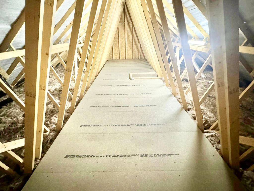 A CB Lofts installation: pale moisture-resistant P5 boards laid on raised loft legs between the timber trusses of a Cambridge home